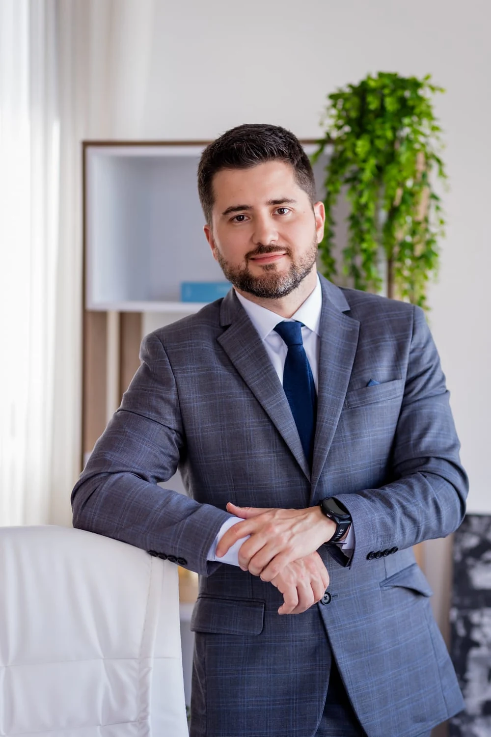 Dr. Rafael de Matos de terno, apoiado em uma poltrona no consultório