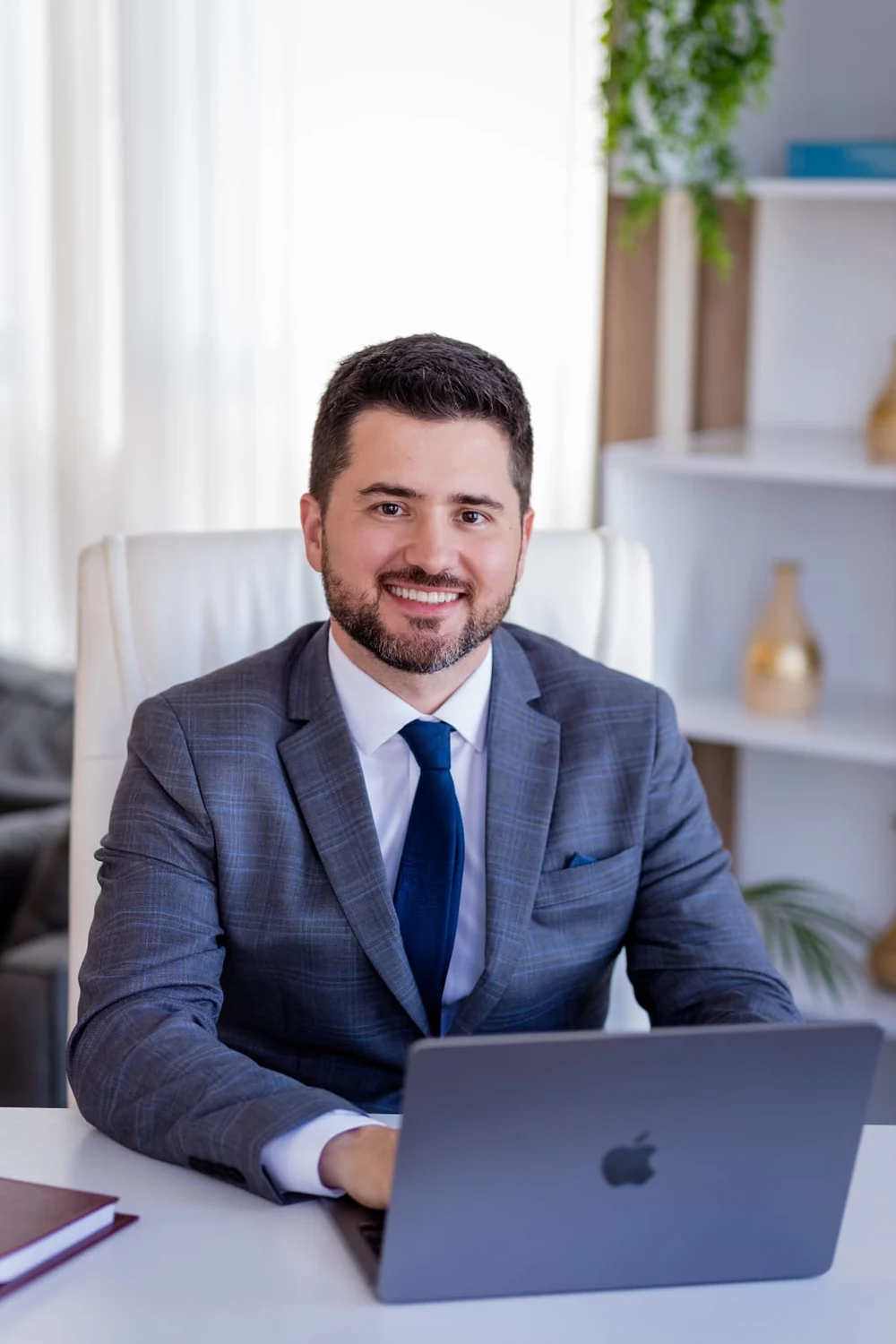 Dr. Rafael de Matos sentado à mesa do consultório, sorrindo, com um notebook aberto