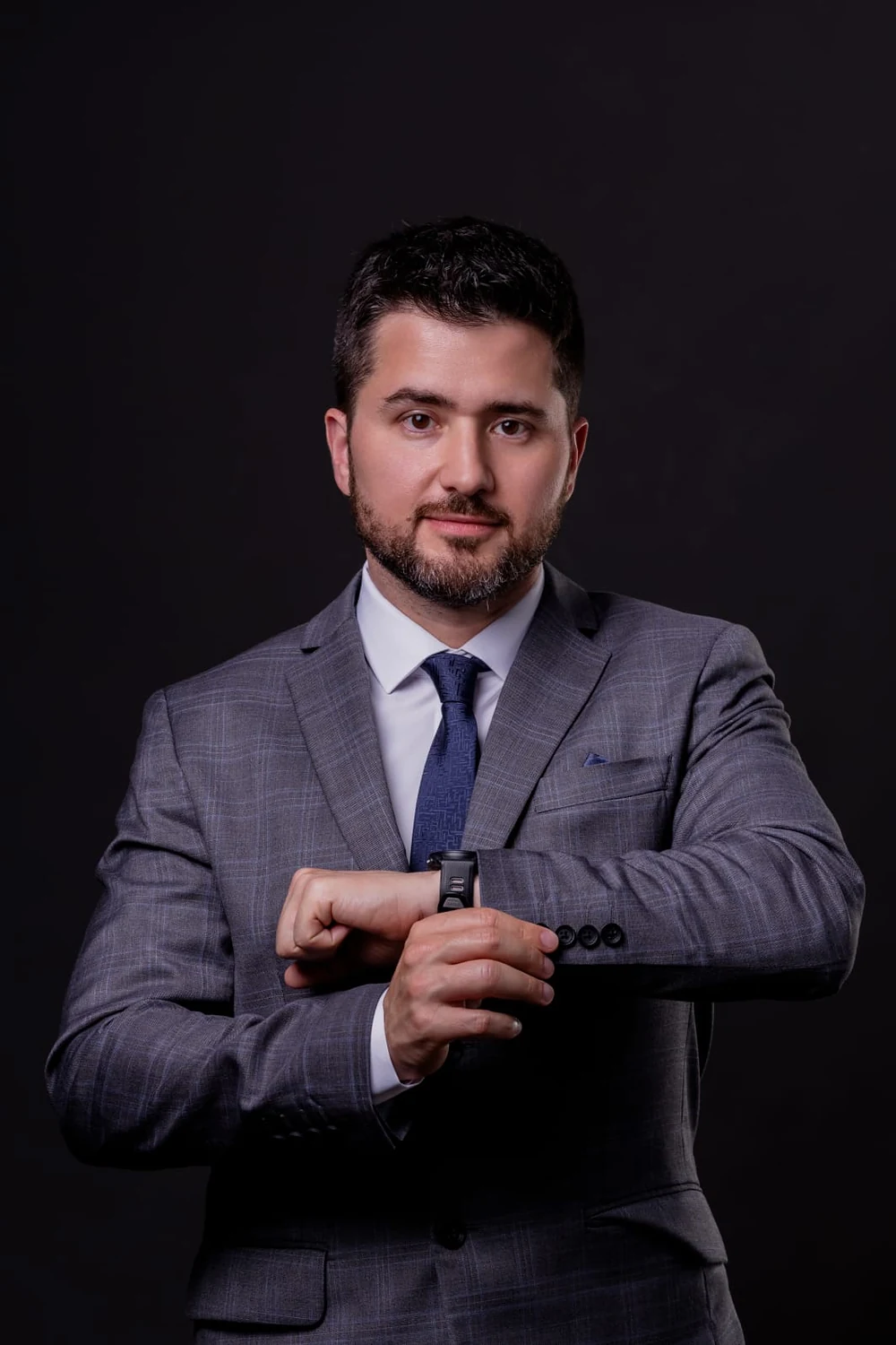 Dr. Rafael de Matos de terno cinza, ajustando o relógio, em retrato com fundo escuro